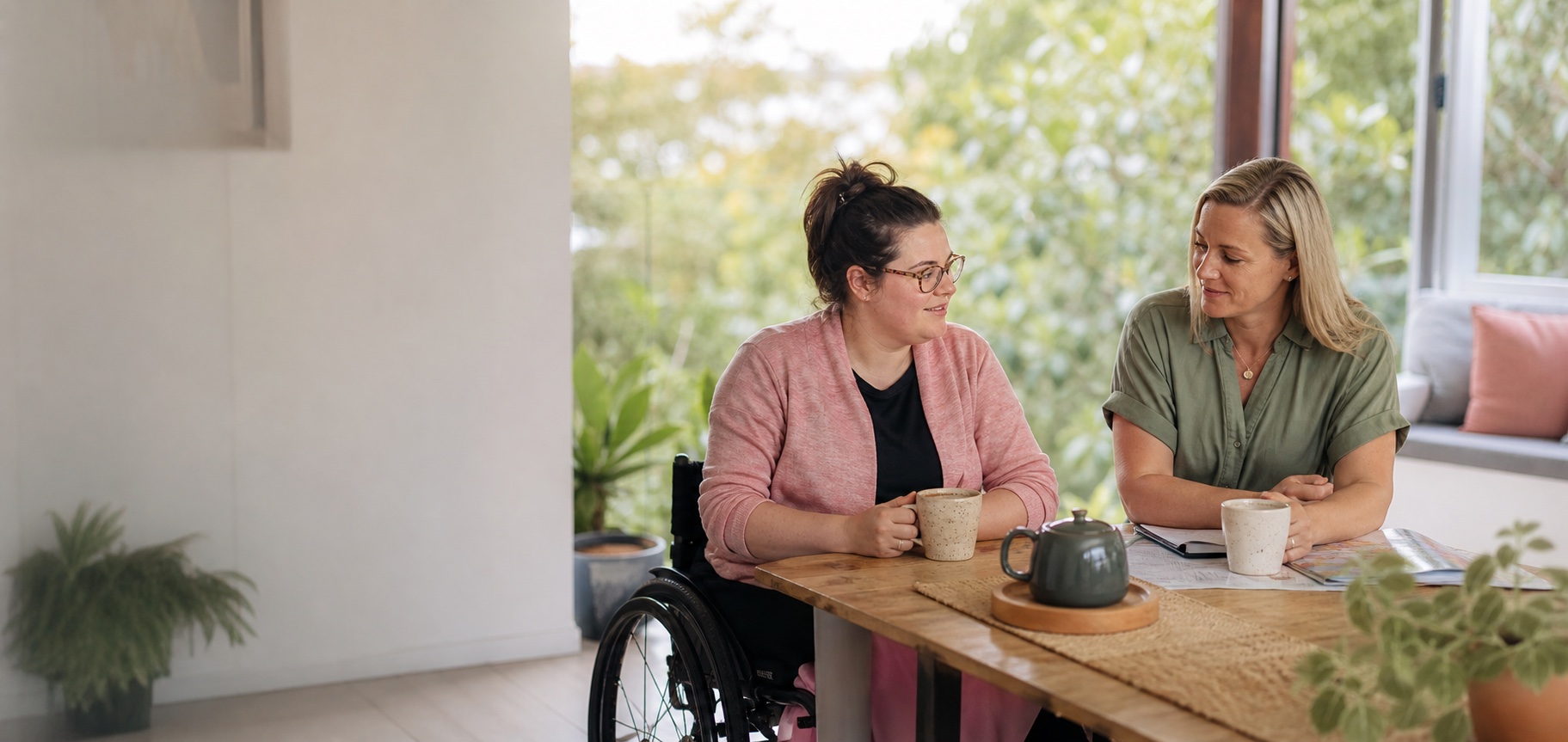 A wheelchair user talking with her support worker over tea at home